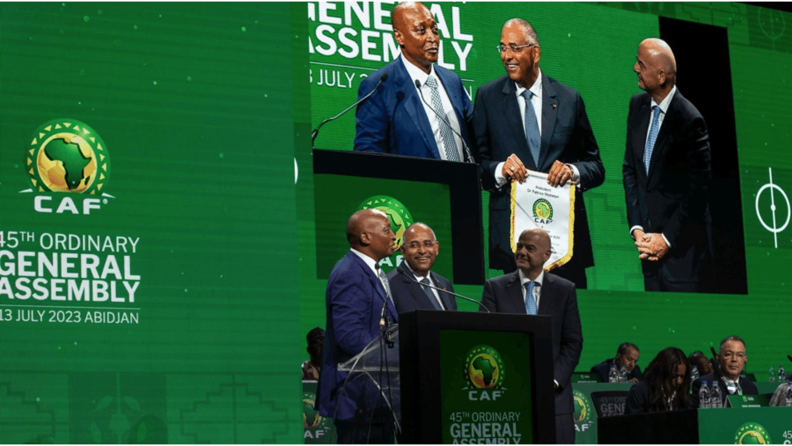 Patrick Achi shakes hands with the CAF President at a formal event, applauding his contributions to African football development.